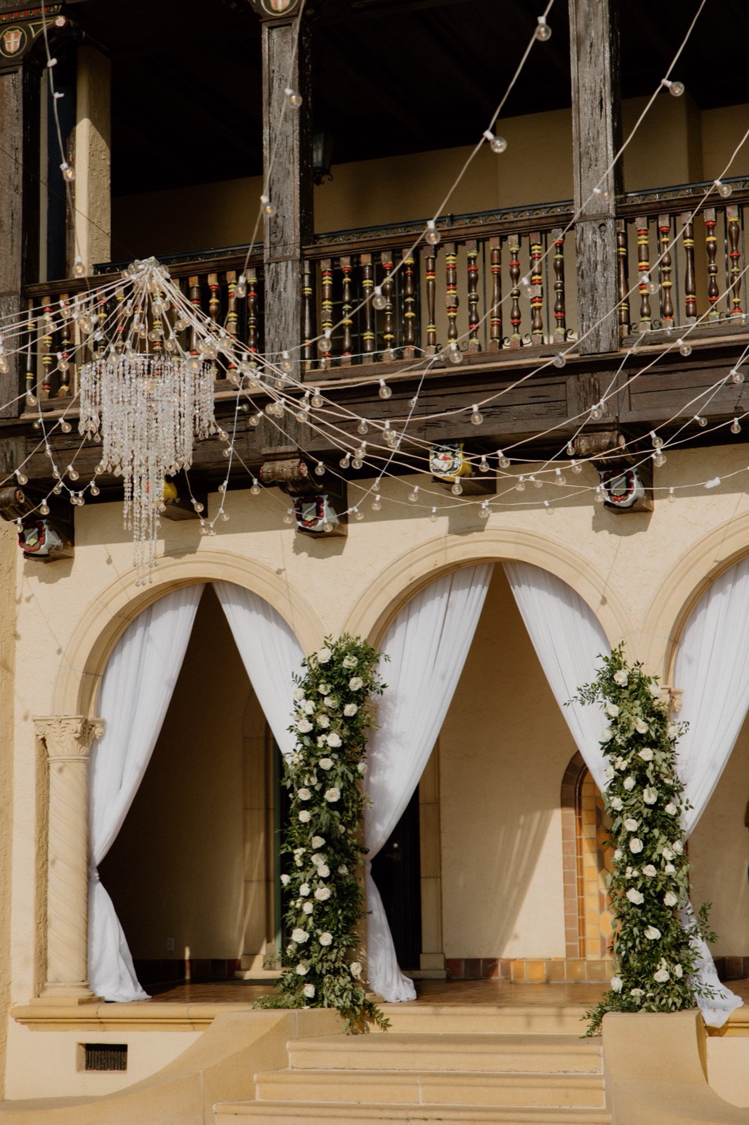 Historic venue ceremony entrance with white draping, floral columns, and string lights