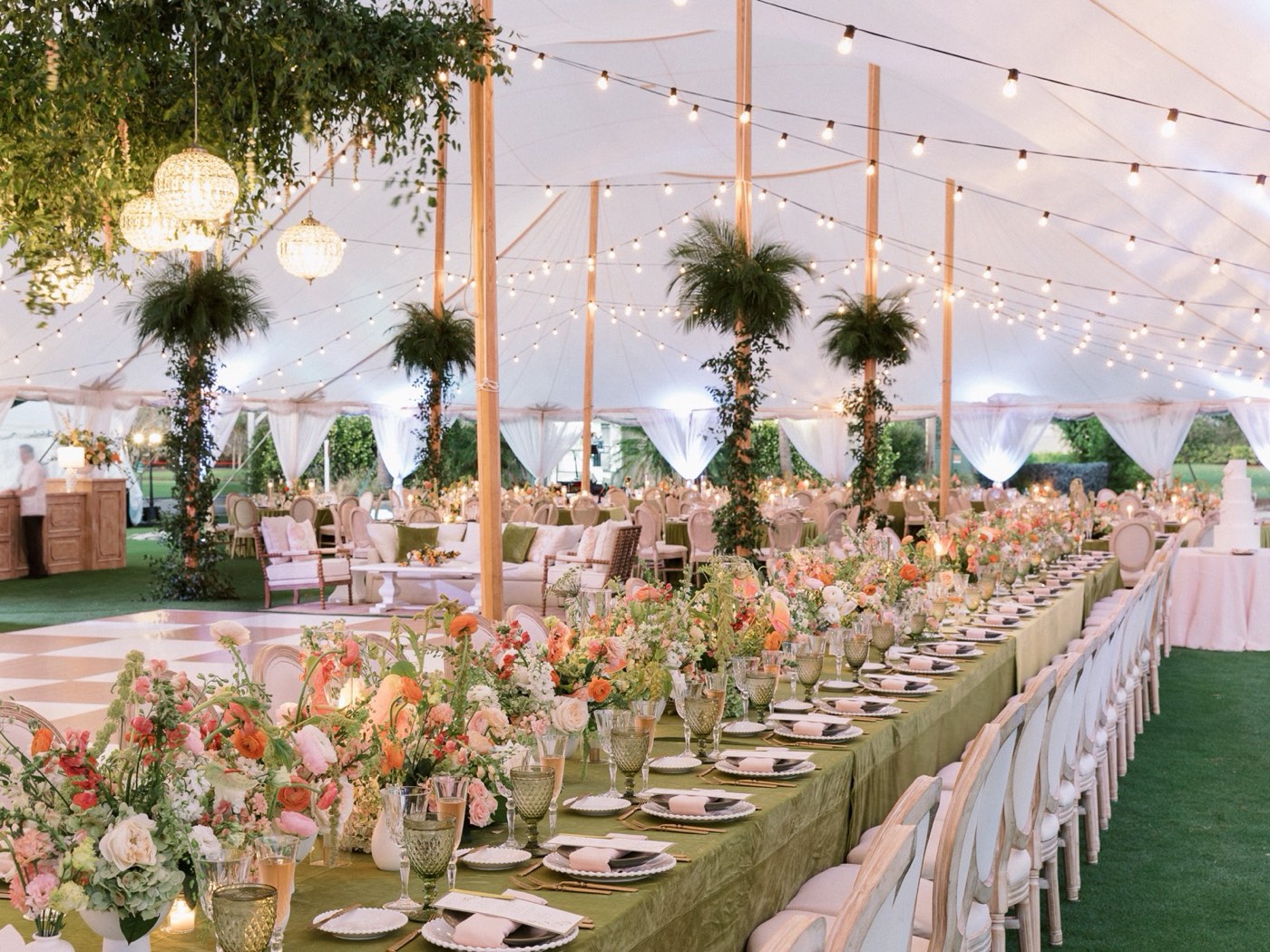 Tent reception with floral tablescape, chandeliers, and warm string lighting